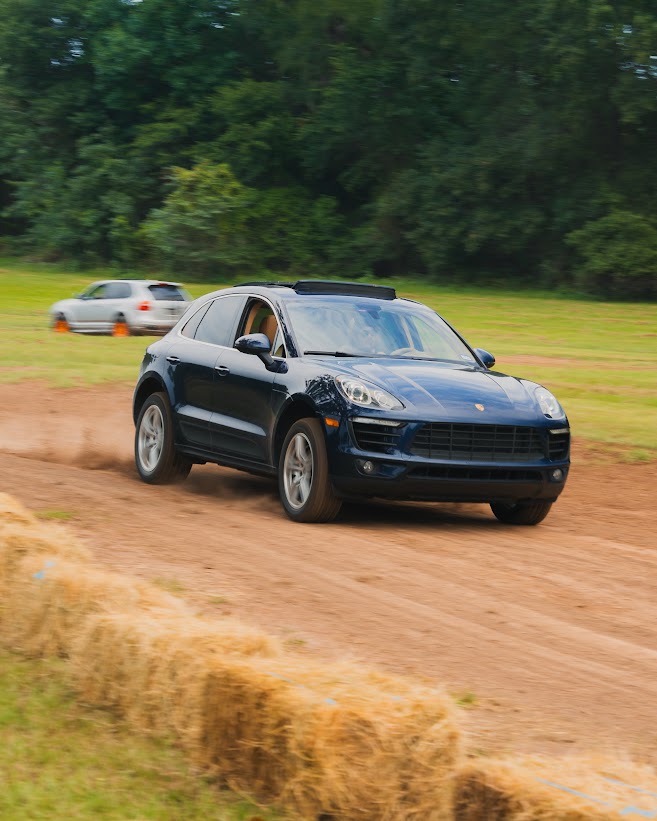 Dark blue Porsche Macan driving a dirt course lined with hay bales