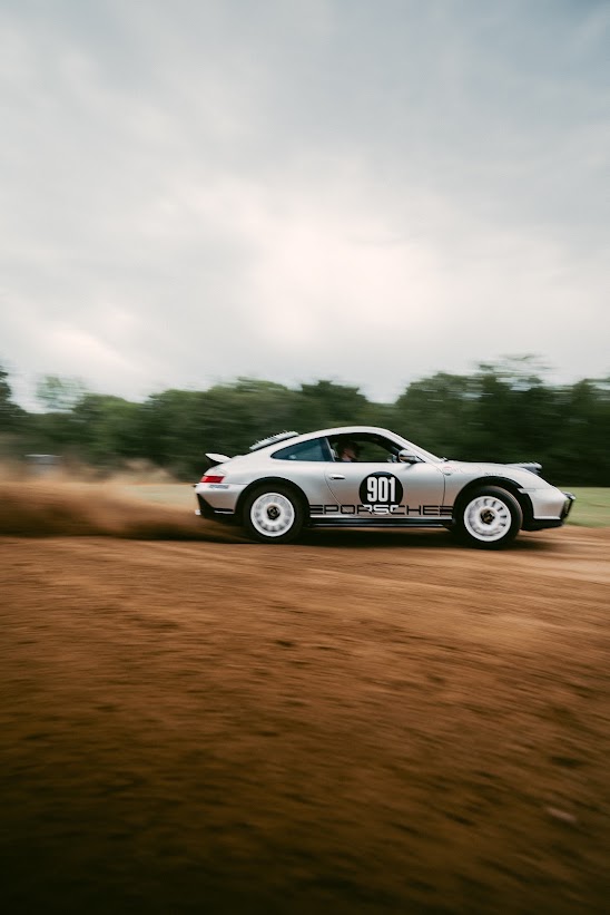 Silver Porsche 911 Safari RS with white rally wheels, seen side-on at speed on a dirt road